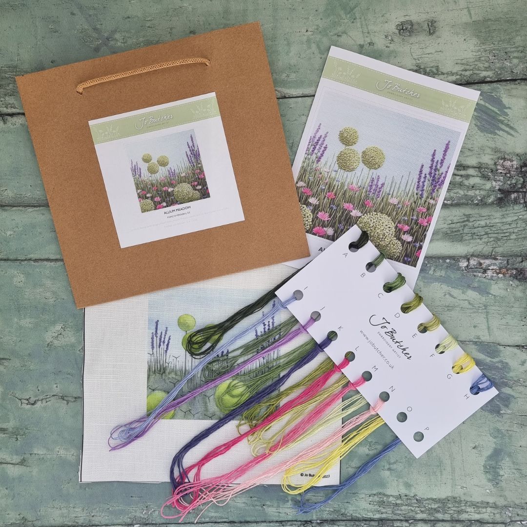 the contents of the Allium Meadow hand embroidery kit by Jo Butcher. Including thread card with 14 different colour threads. printed cotton/linen background, instruction sheet and brown paper bag