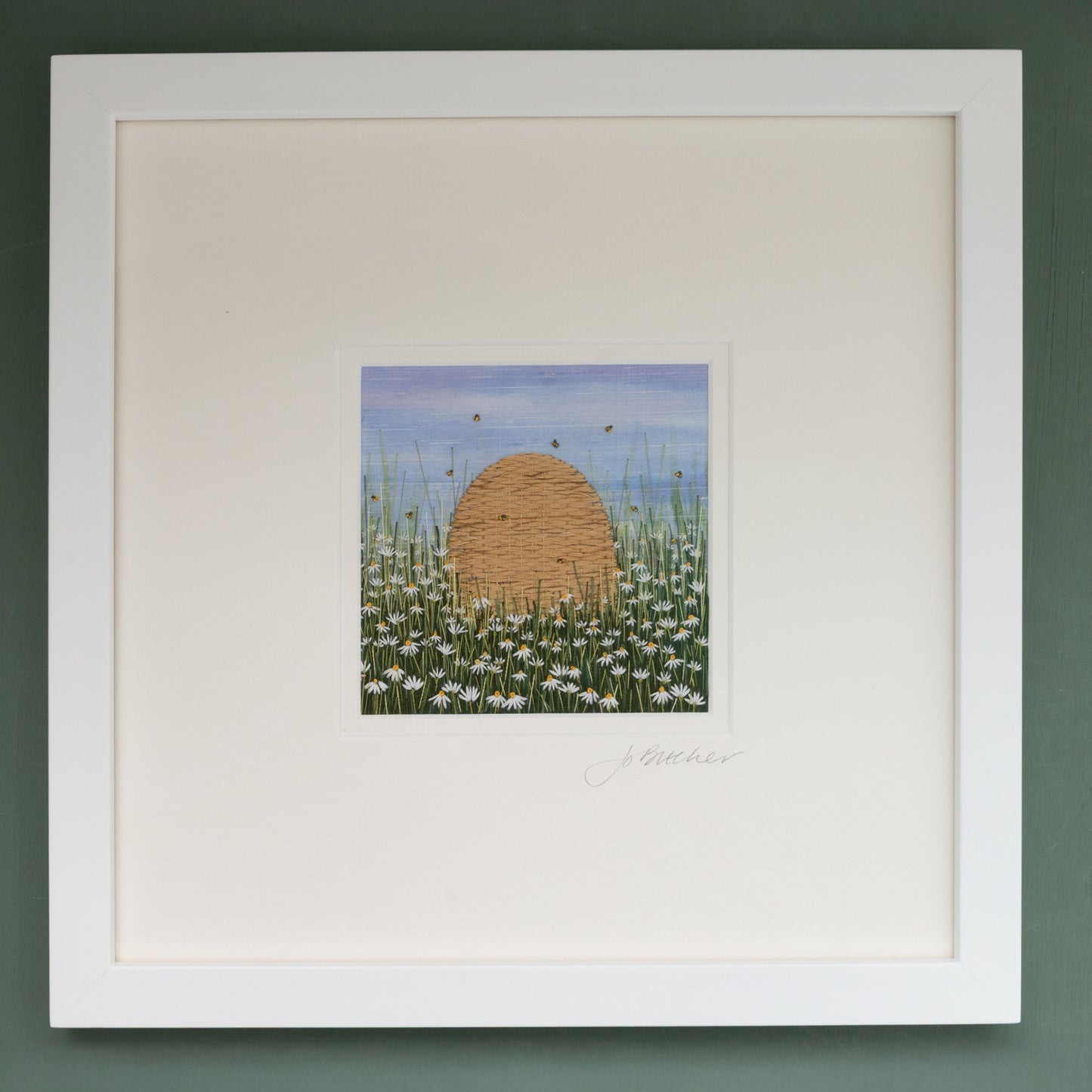 Framed embroidery artwork of a bee skep in a field with of white diasies.