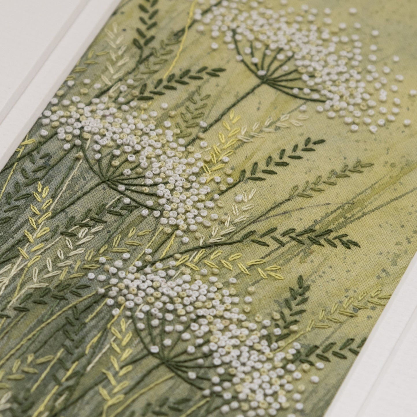 close up of yellow/green hand painted background with embroidered cow parsley and grasses