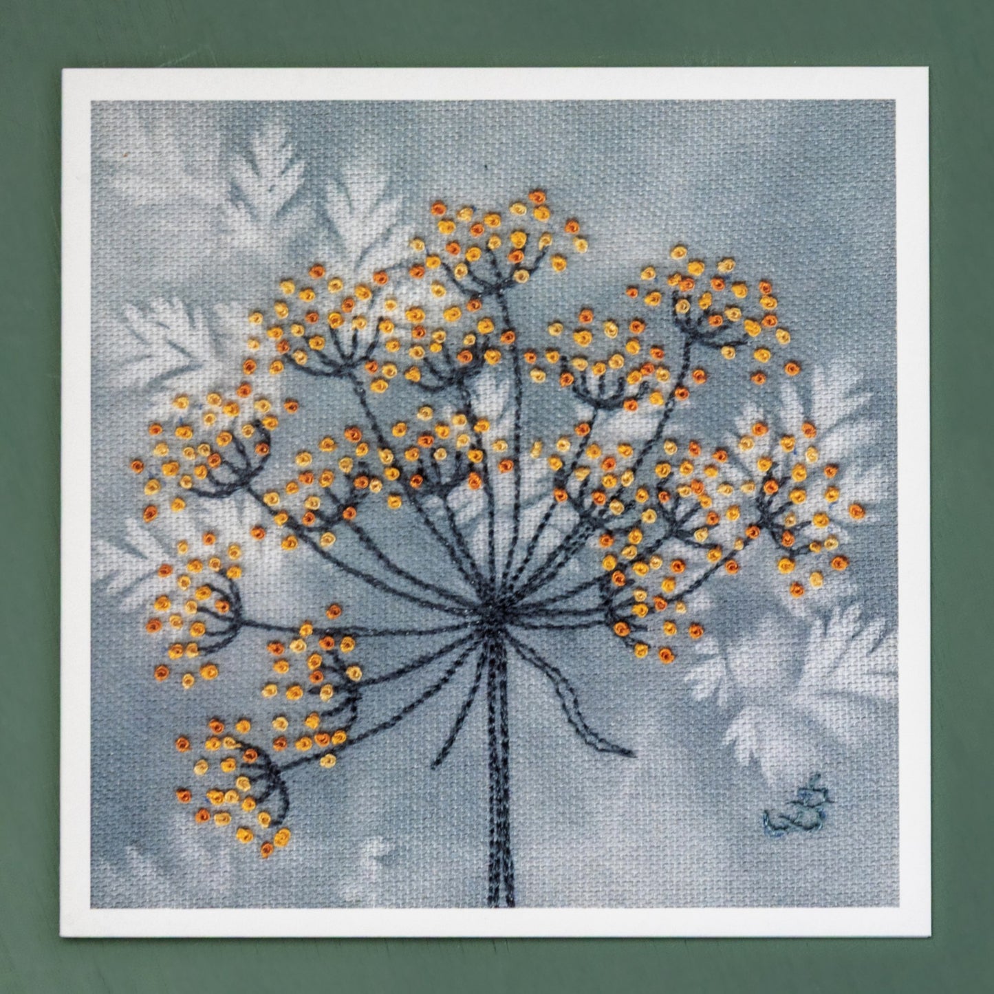 A card of a hand embroidered cow parsley seed head. The dried seed head is depicted using muted orange and yellow French knots on a pale grey background.