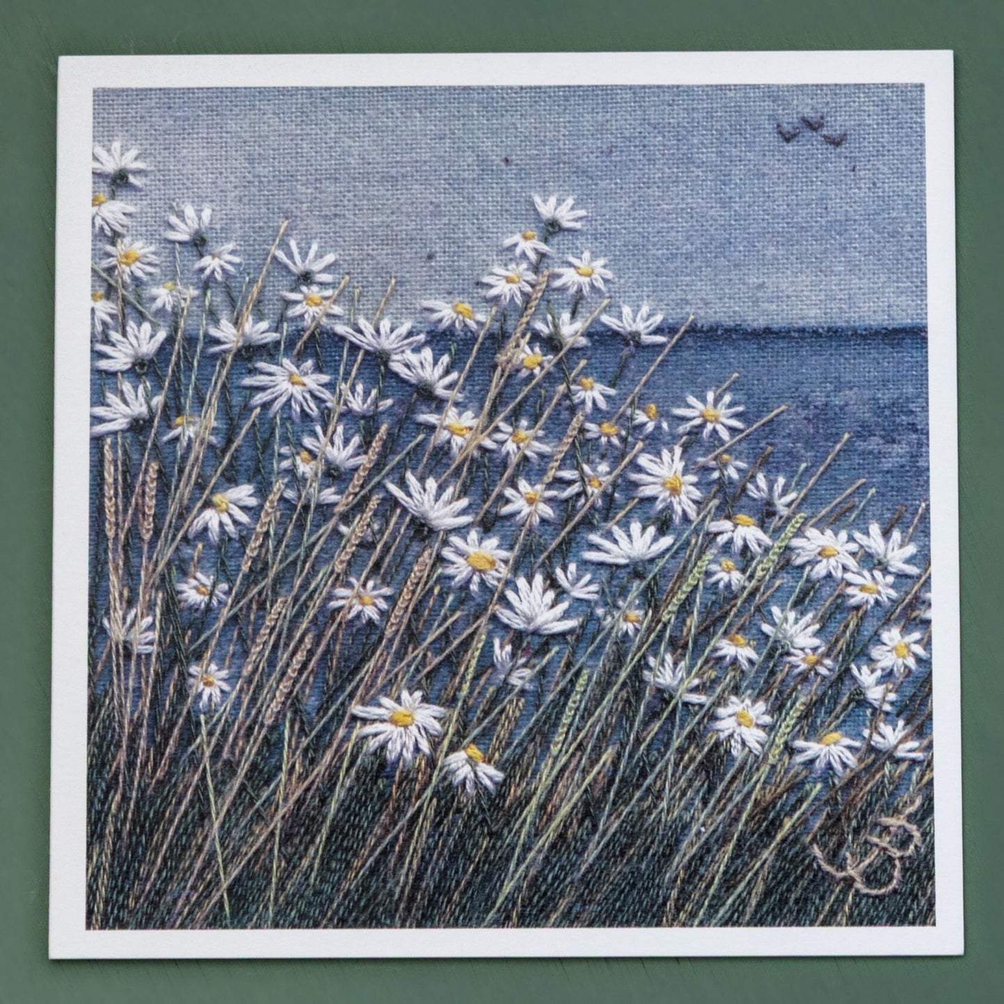this card is of a coastal scene with a painted horizon and a daisy meadow foreground. Three birds can be seen flying in the distance.