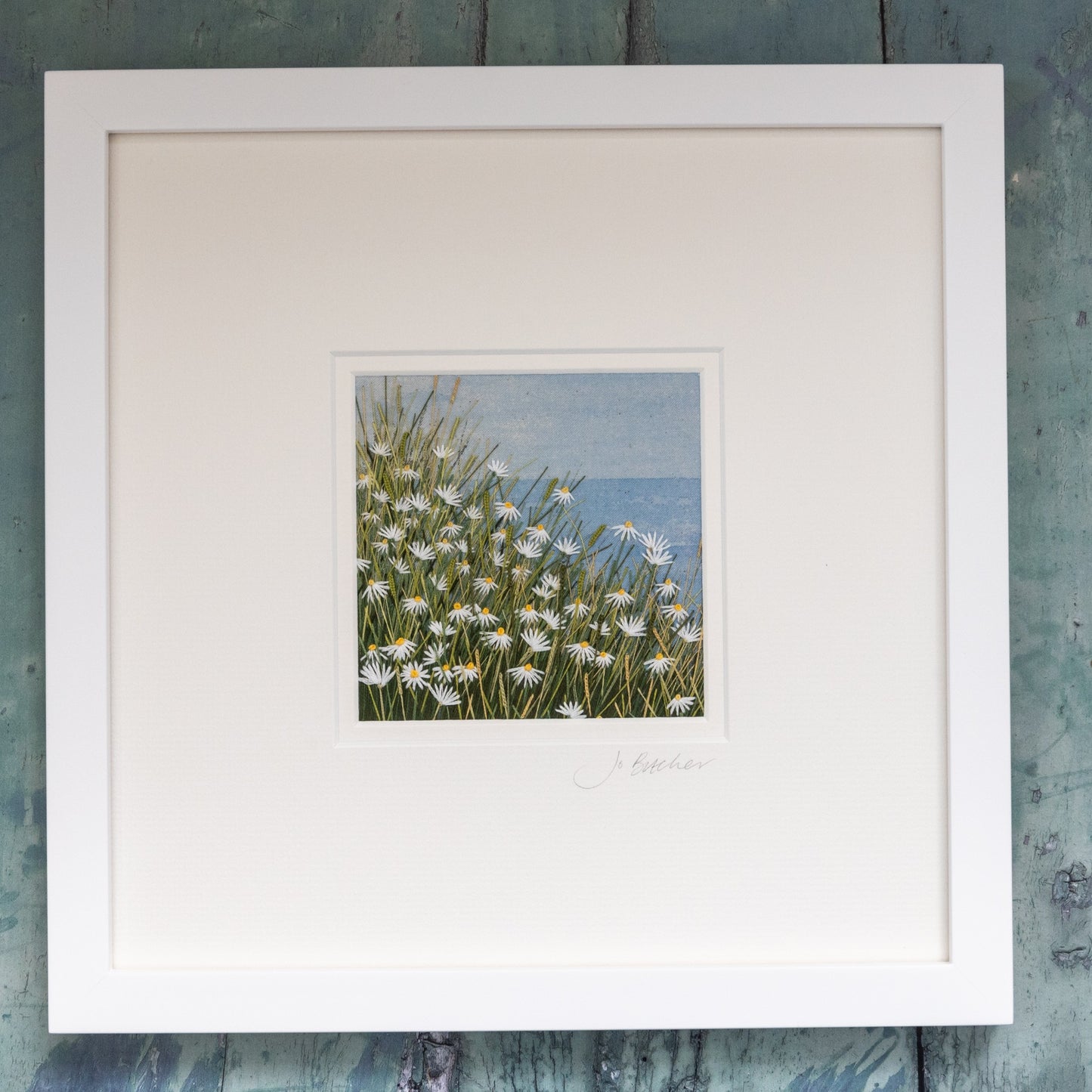 Framed embroidered artwork of daisies by the sea.