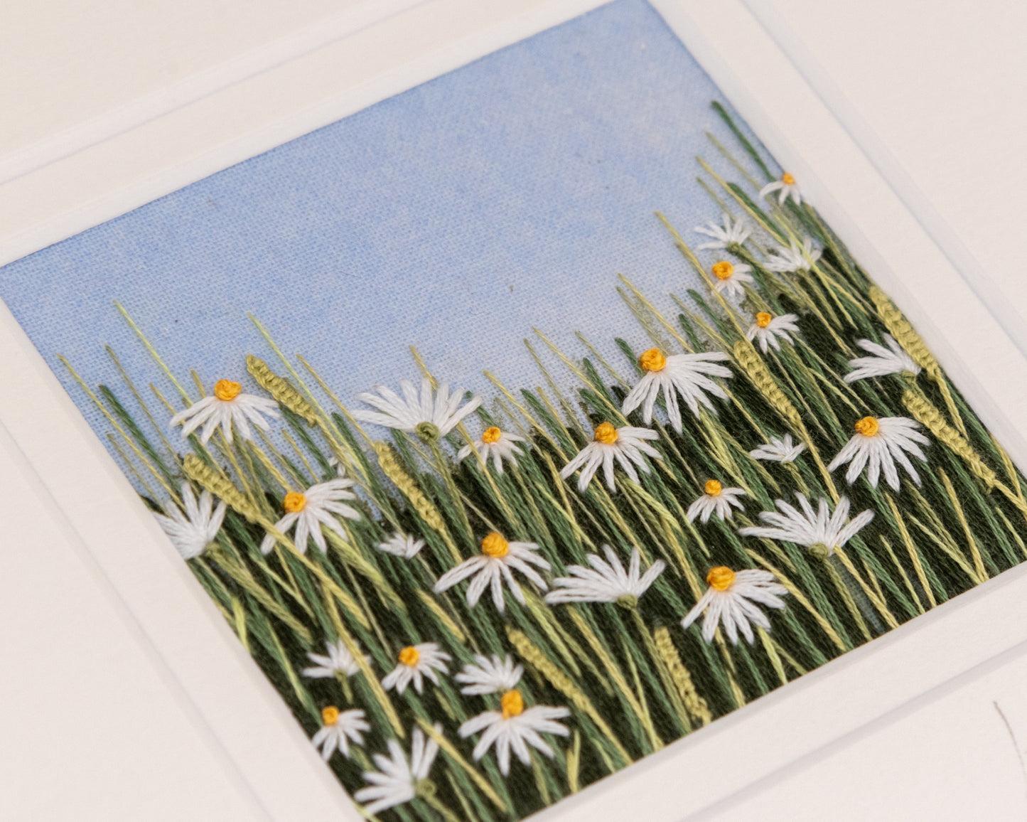 close up view showing the stitching detail of the flowering white daisies in amongst the grasses.