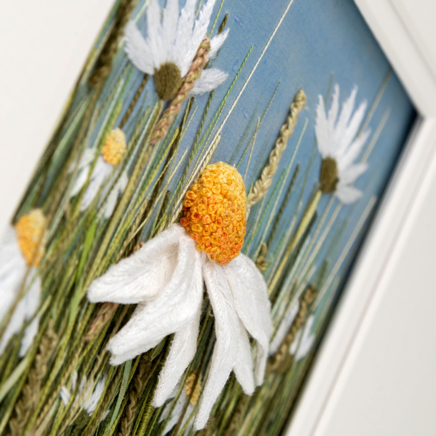 A large white stumpwork daisy protrudes from the painted background with embroidered grasses and other daisies.