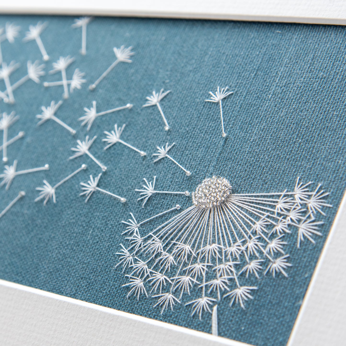 Close up of the embroidered dandelion clock showing the glass beads and white cotton threads.