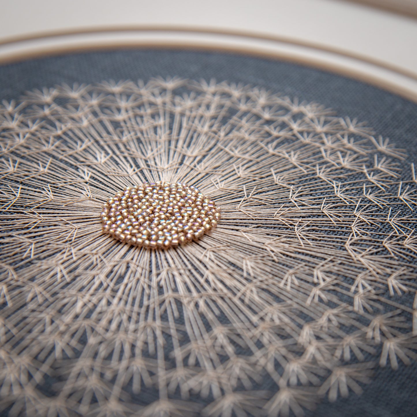 Close up of a hand embroidered dandelion clock.  The centre is glass beads representing the seeds and radiating out are fine silk threads depicting the papus