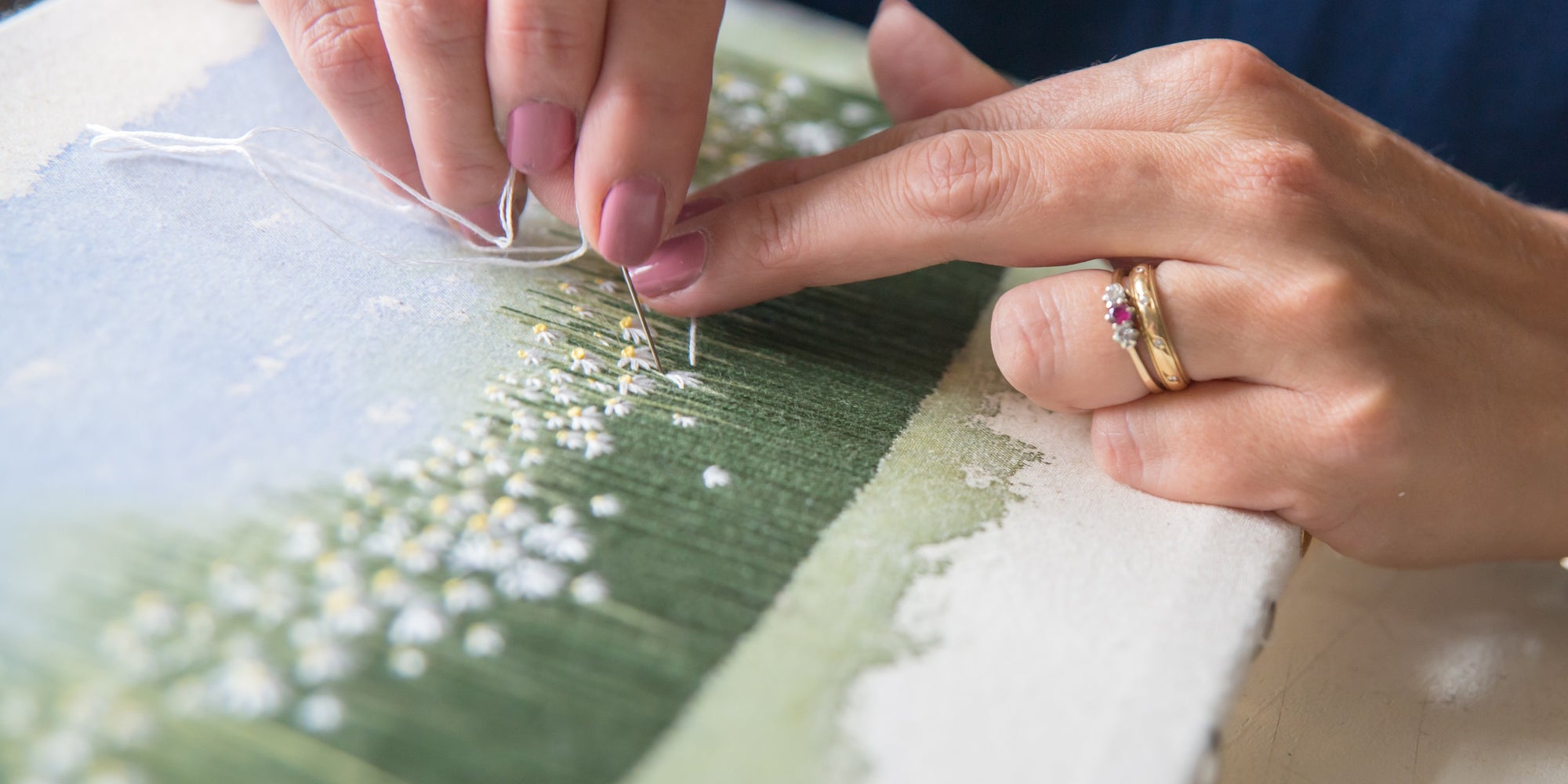 Jo's hands sewing white daisies onto a green stitched background to show how her artworks are built up.