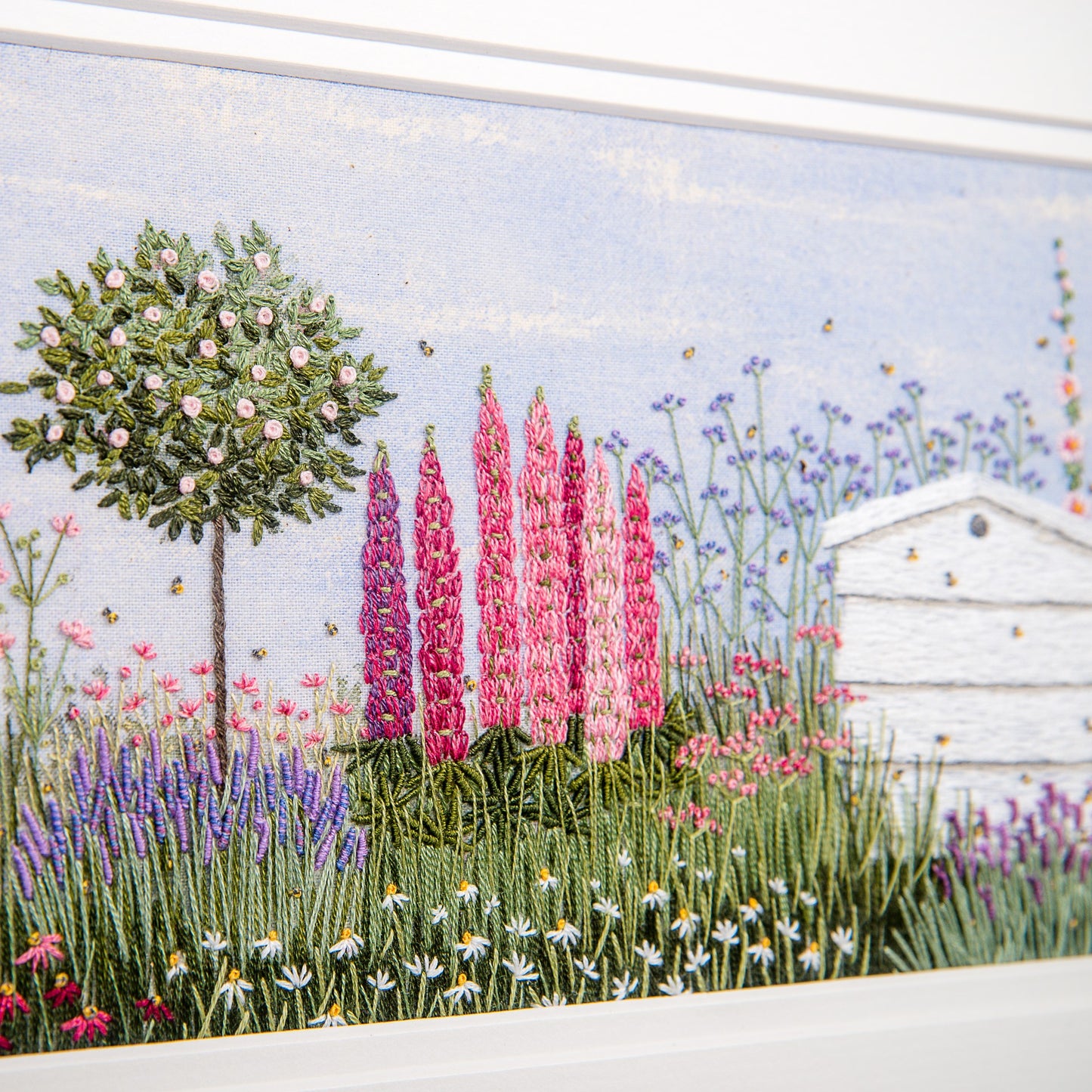 close up of the pink standard rose, lupins and the beehive showing stitching details.