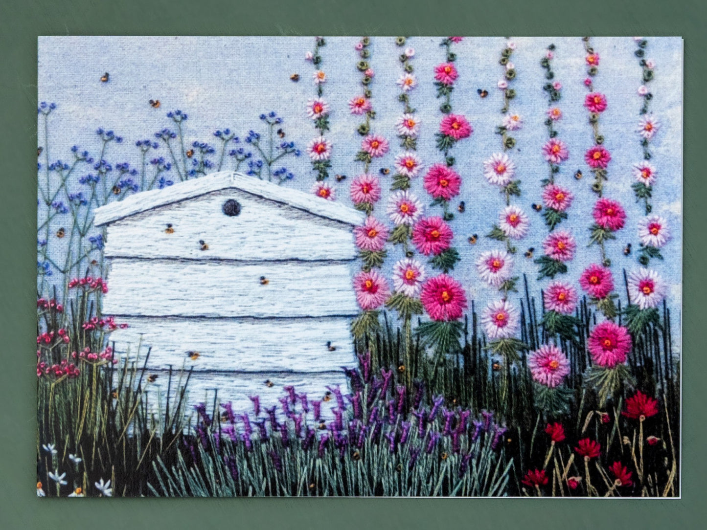 A hand embroidered white bee hive is the main feature if this card.  The bees are flying around the hive and the surrounding flowers.