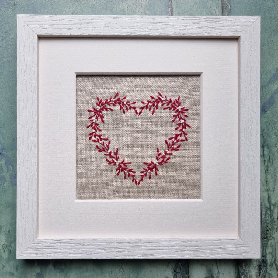 This embroidery kit is a heart stitched of red leaves and white berries on a beige linen background