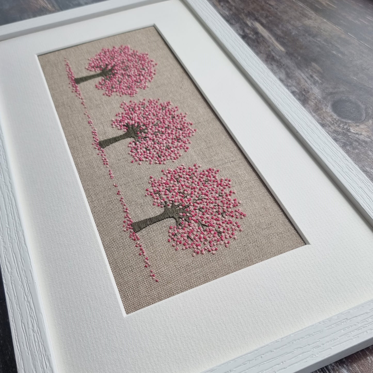 Three embroidered cherry blossom trees framed in a white frame.