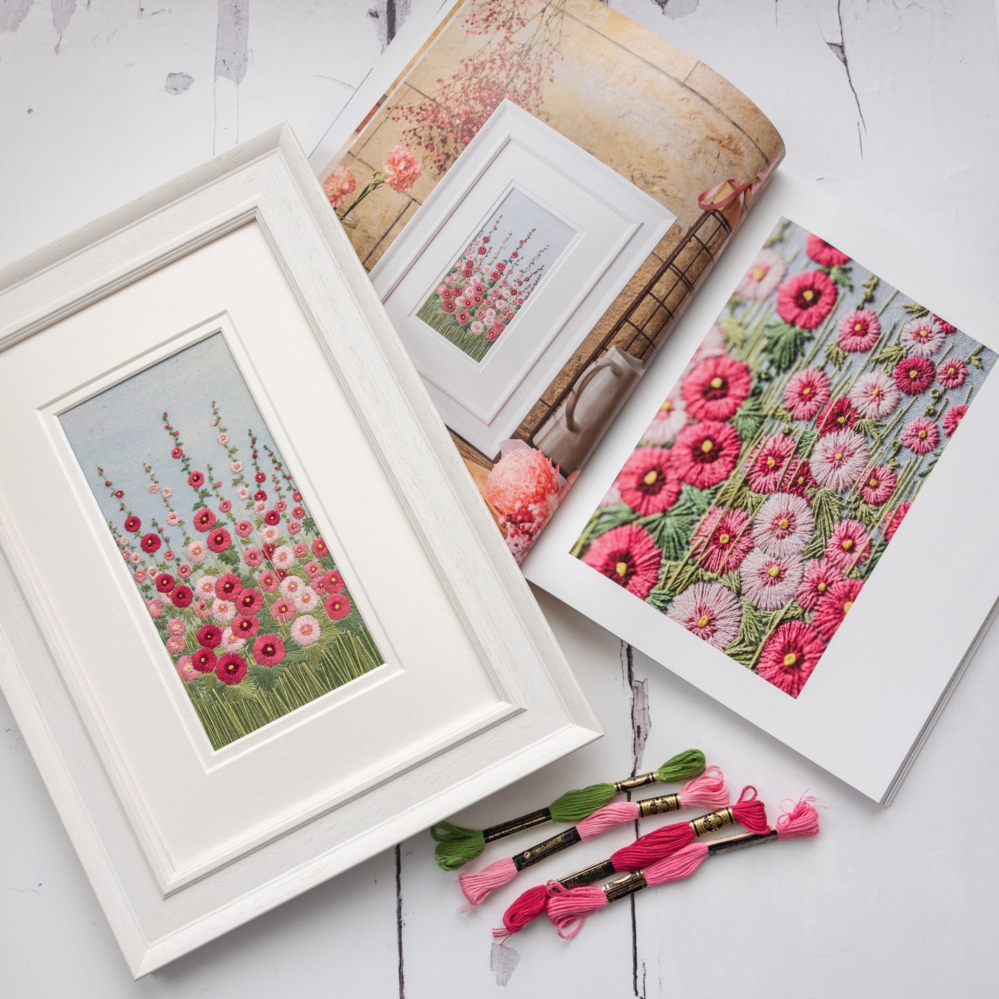 The original hand embroidered artwork of Hollyhocks sits with a few cotton skeins on top of Jo's book open at the right page