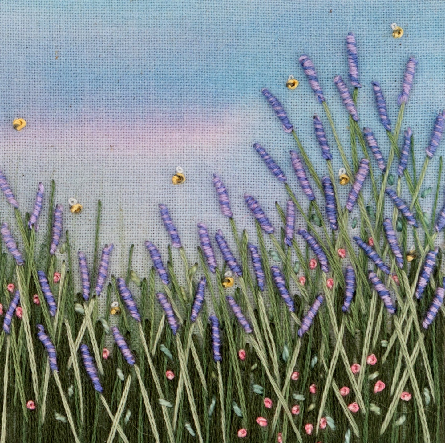 A close up view of a hand embroidered lavender meadow showing the stitch details of the lavender and bees.