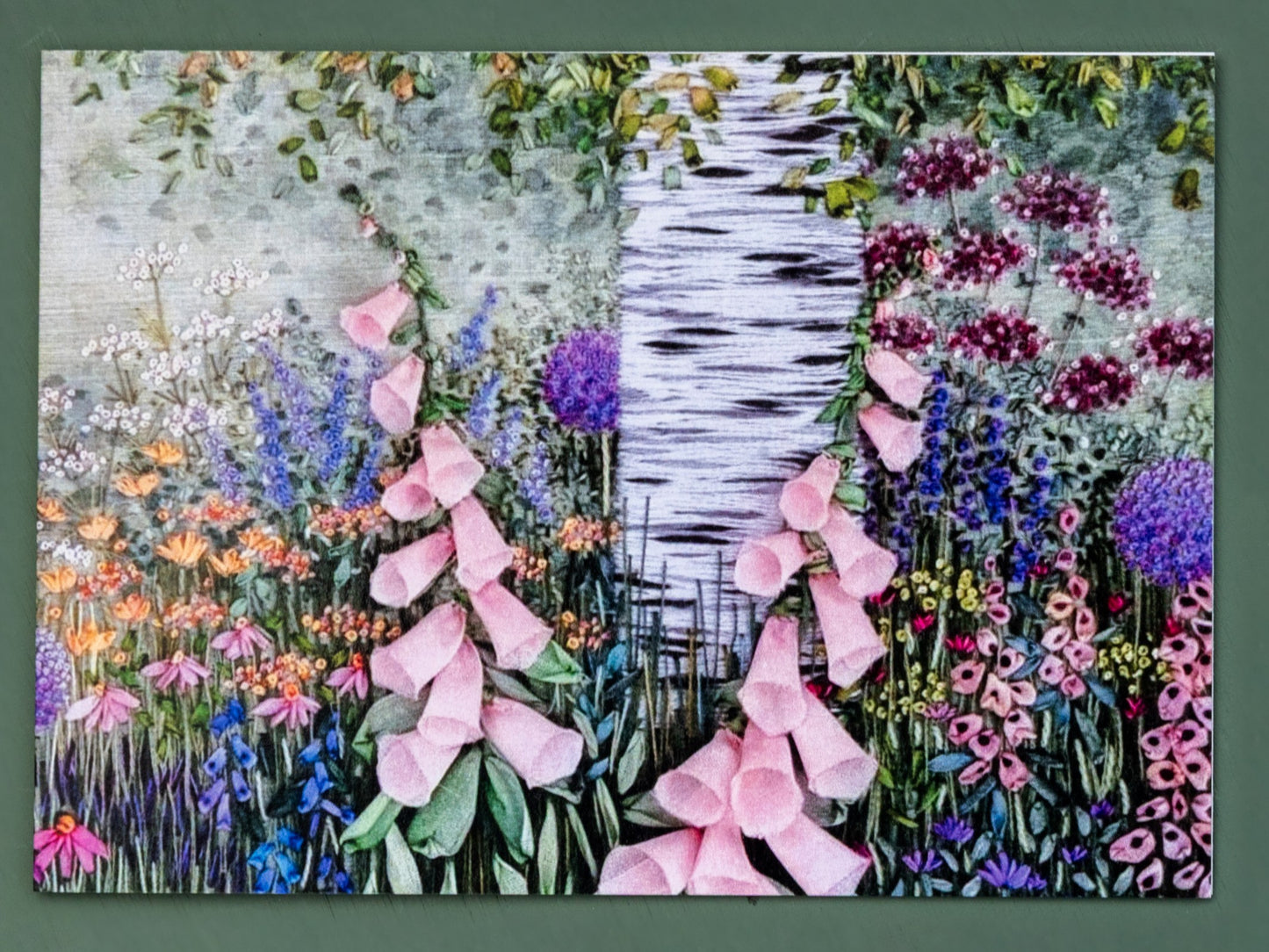 A Card showing the hand embroidered trunk of a silver birch tree. Under the tree is a flower border filled with a range of flowers in full bloom.