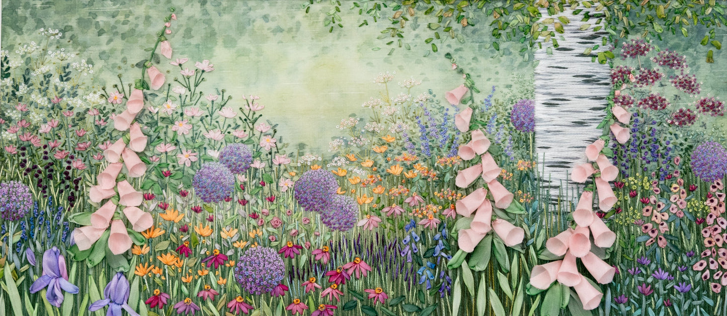 A silver birch tree trunk and lower branches shade a flower border full of pretty flowers