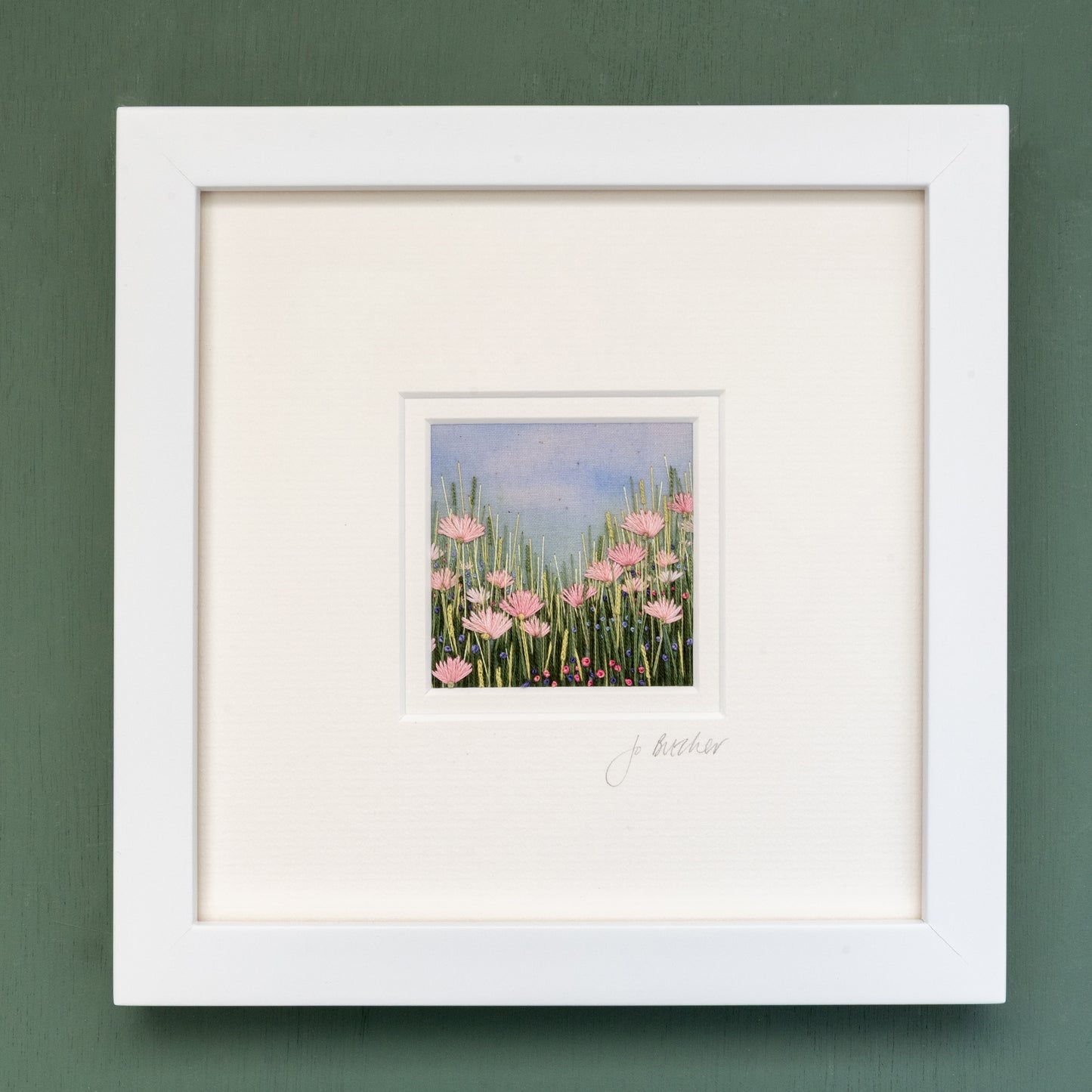 White framed embroidery of a pink flower meadow.