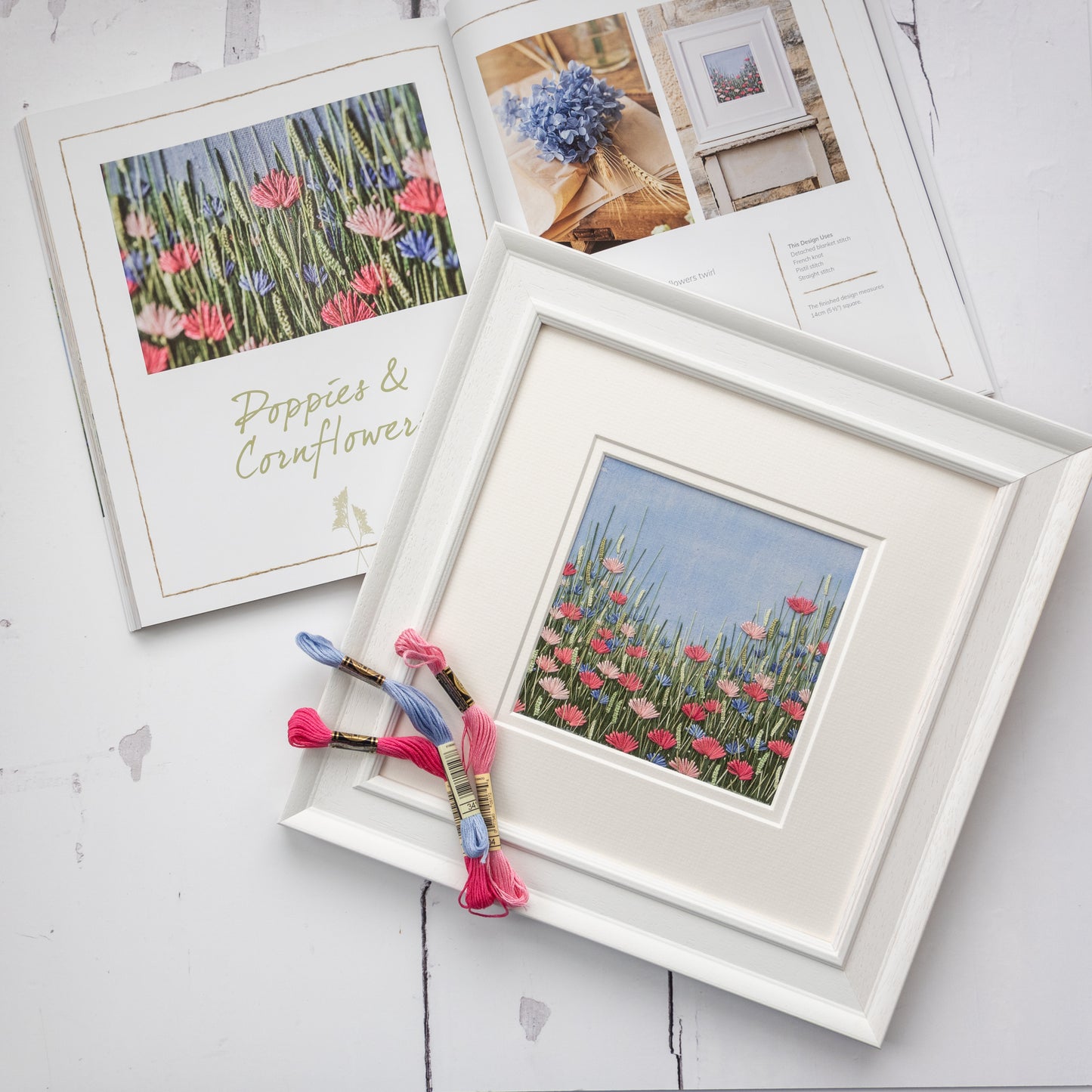 The original hand embroidered artwork of poppies and cornflowers sits with a few cotton skeins on top of Jo's book open at the right page