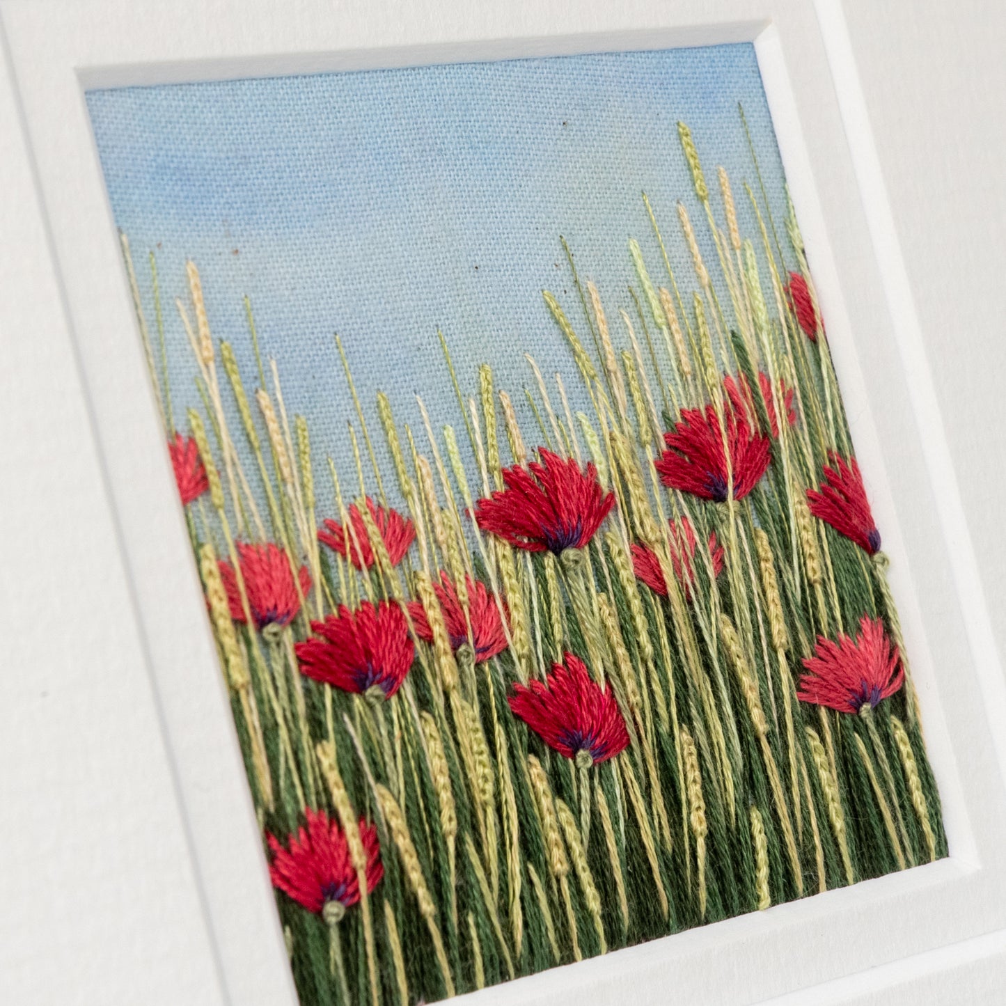 Close up of the stitch detail of the red poppies and flowering grasses.