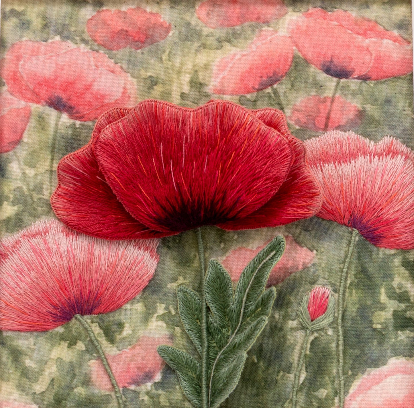 A bright red stumpwork poppy with three petals and a leaf stands out of the page. the background has painted and embroidered poppies give int image real depth.