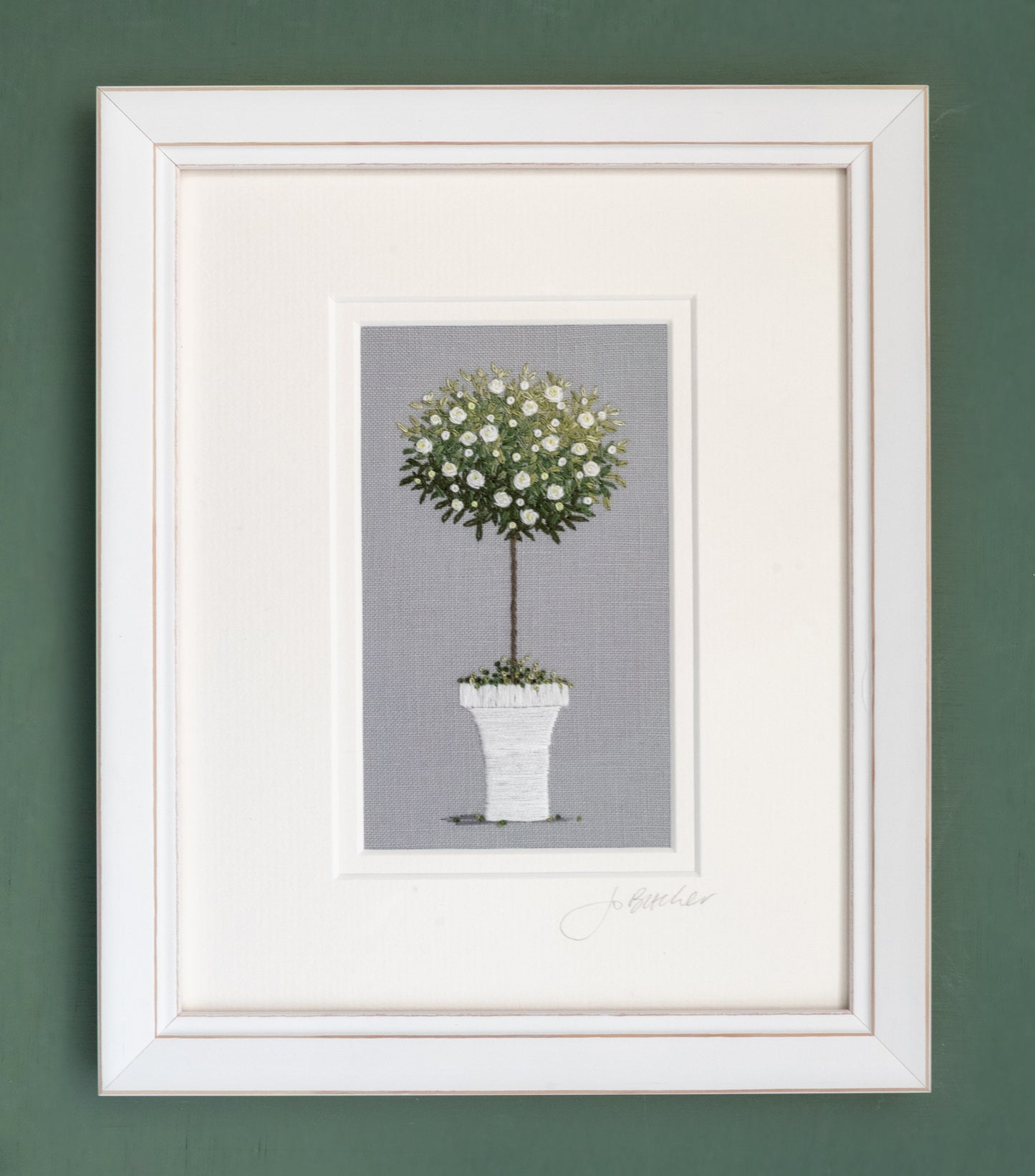 A white framed rose tree on a pale grey cotton/linen background.