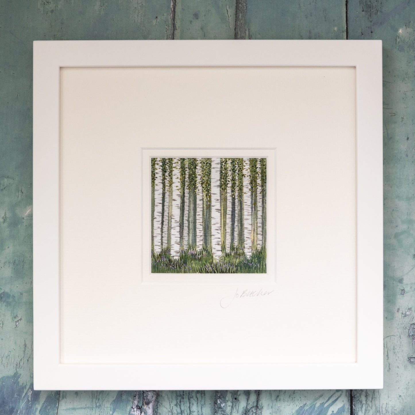 A white framed embroidery of ten Silver birch trees forming a glade. Grasses and blue flowers surround the base of the trees.