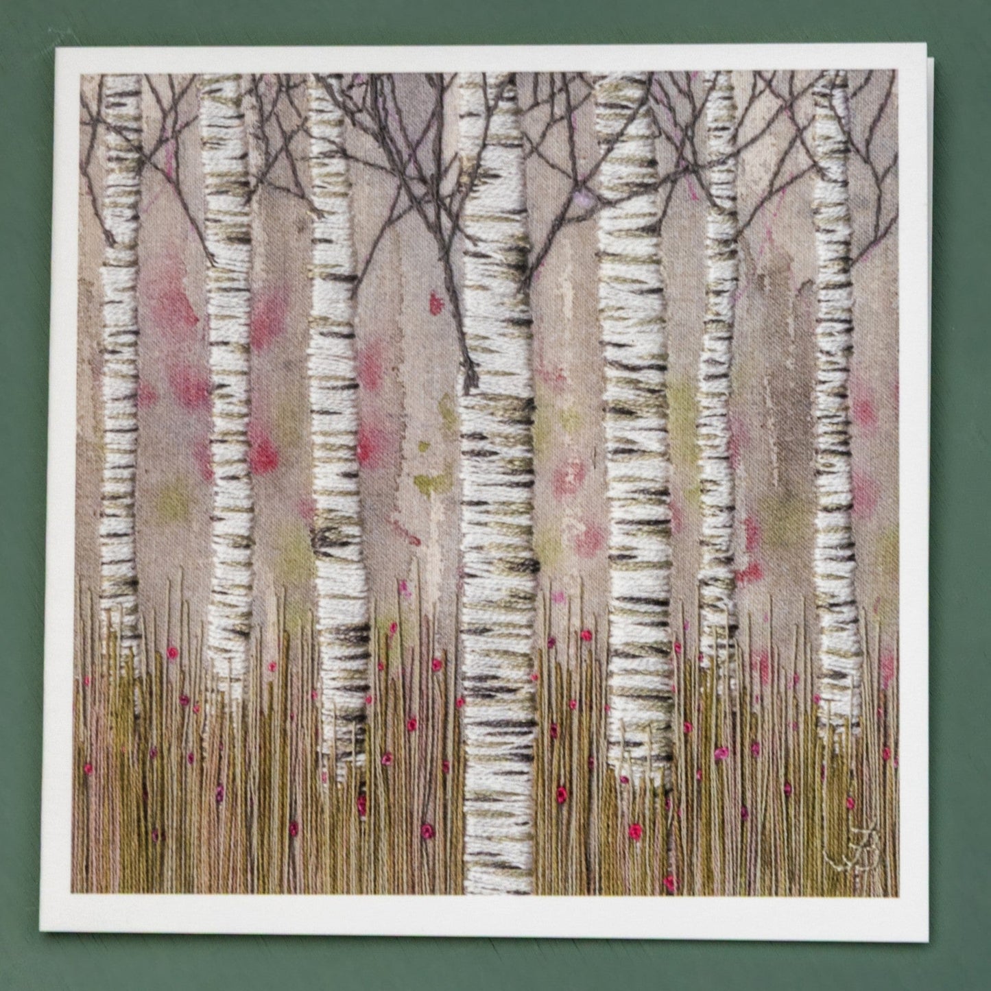 A hand embroidered glade of seven silver birch trunks rise above the grasses with pink flowers hiding in the grass.