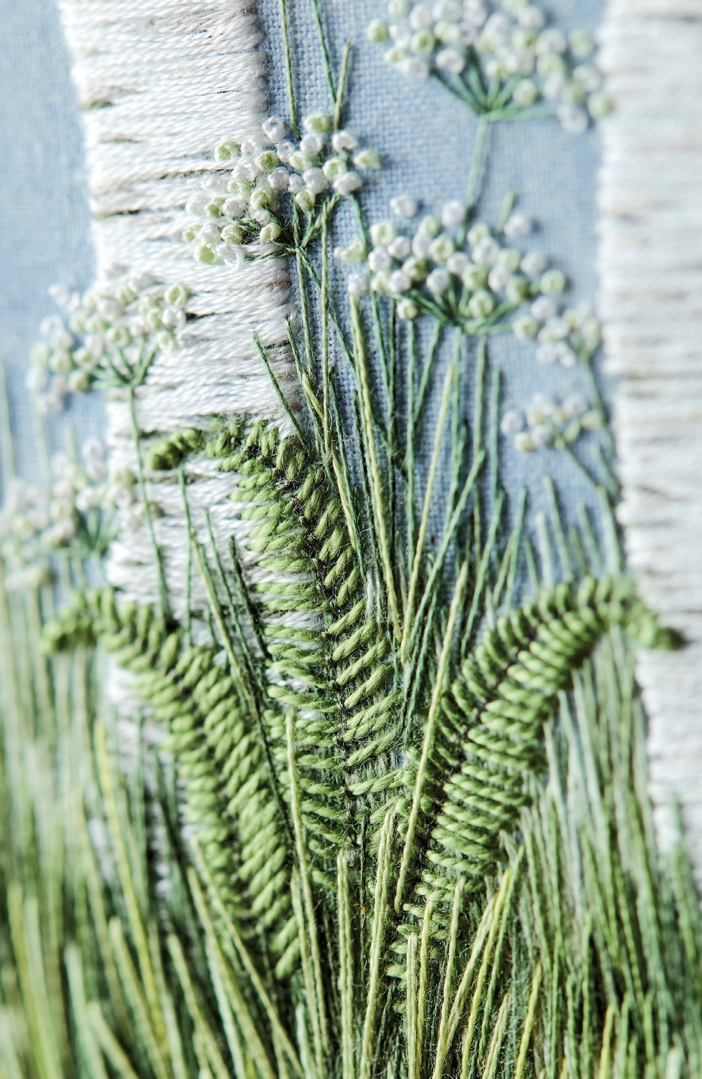 close up view of hand embroidered artwork of the bottom of a pair of silver birch trunks with cow parsley, ferns and grass