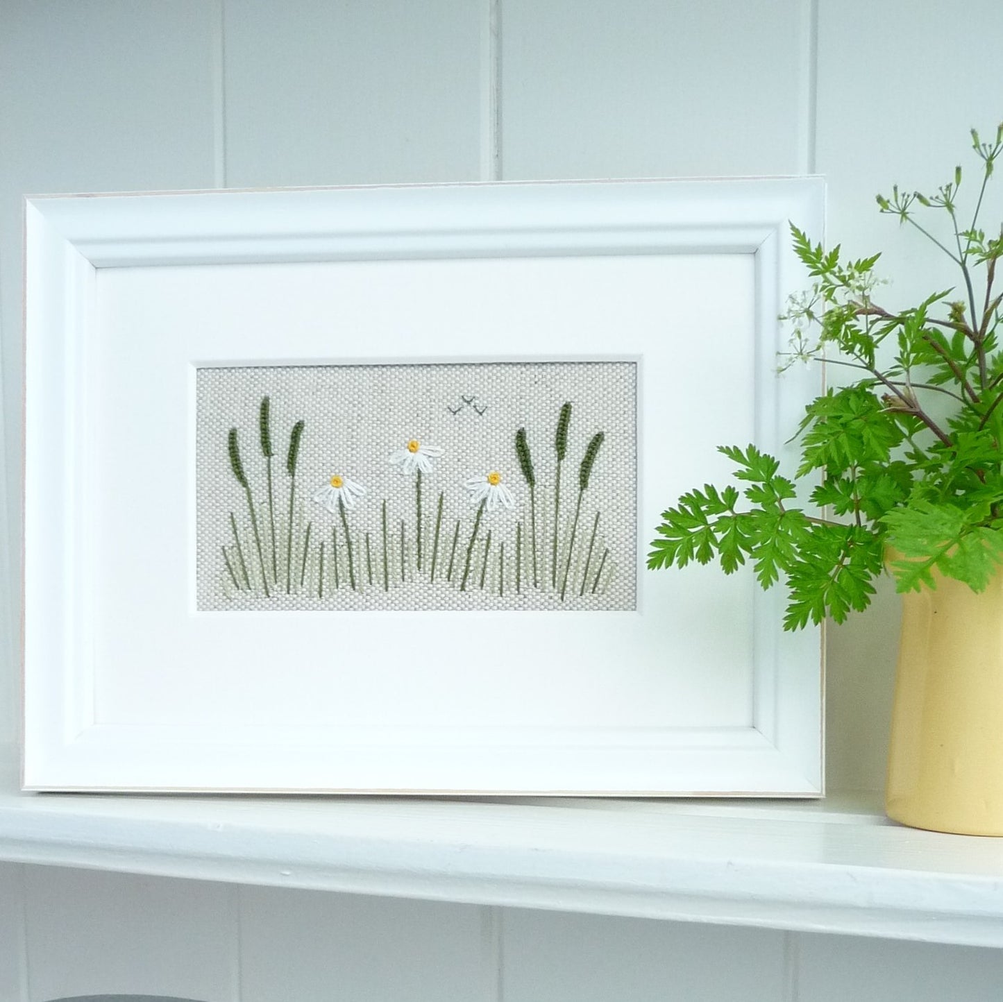 the framed completed kit staged on a shelf with a vase of mixed foliage.