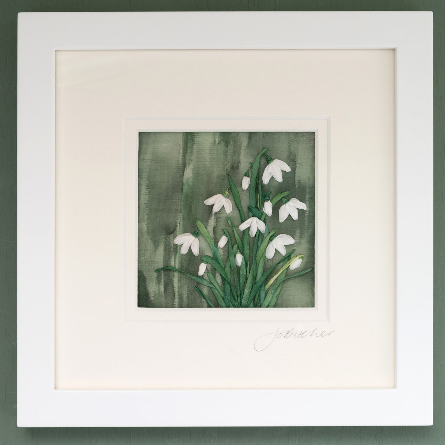 A clump of snowdrops hand embroidered using hand dyed silk ribbons on a painted green speckled background.