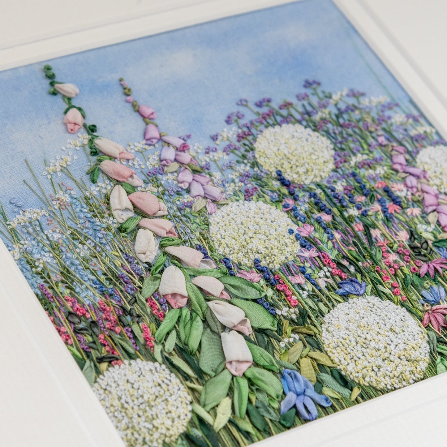 square artwork of a flower border in close up featuring  foxglove spires embroidered using hand dyed silk ribbons and other flowers and foliage including Alliums, irises and Verbena bonairiensis