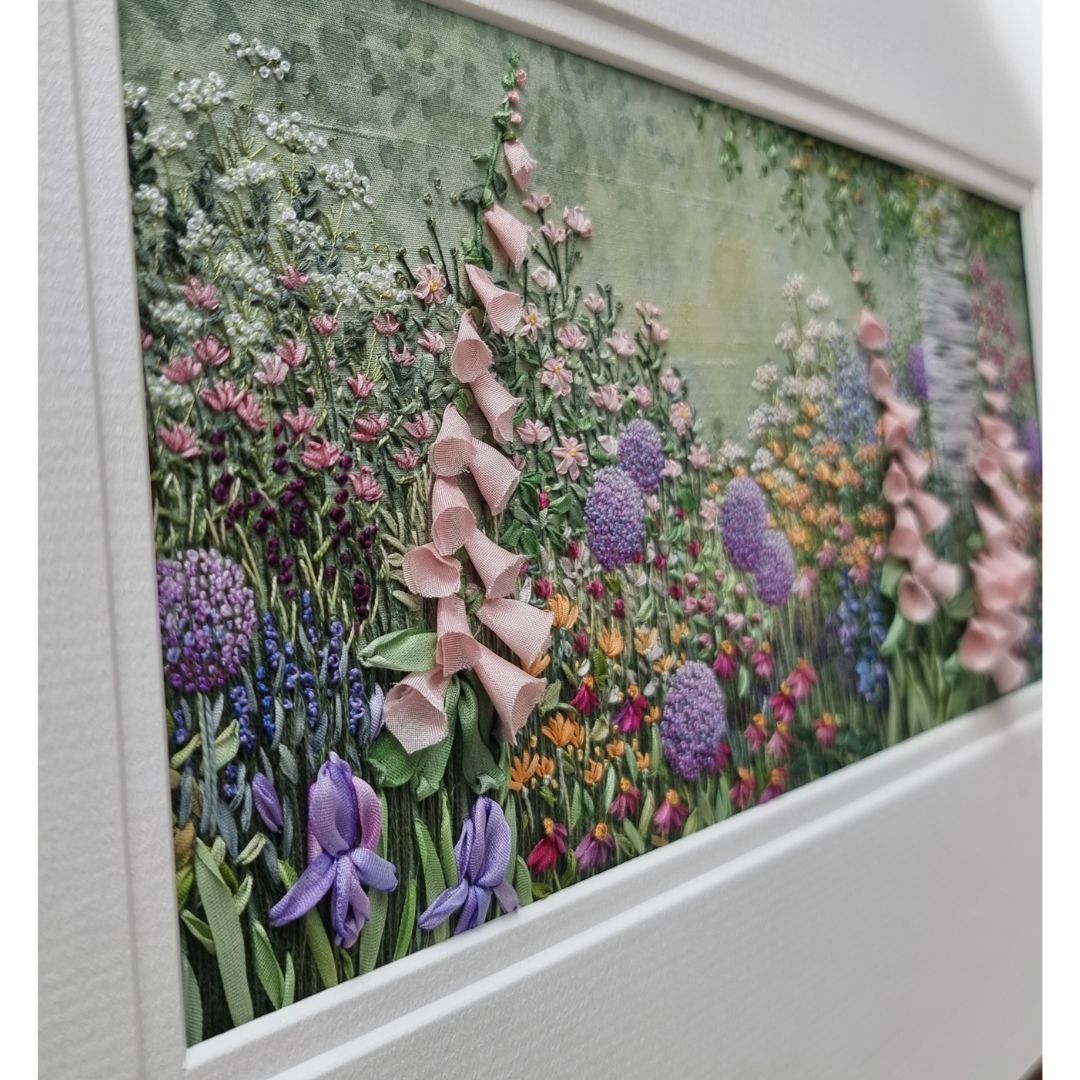 view looking across hand embroidery of pale pink foxgloves and other flowers and a silver birch trunk