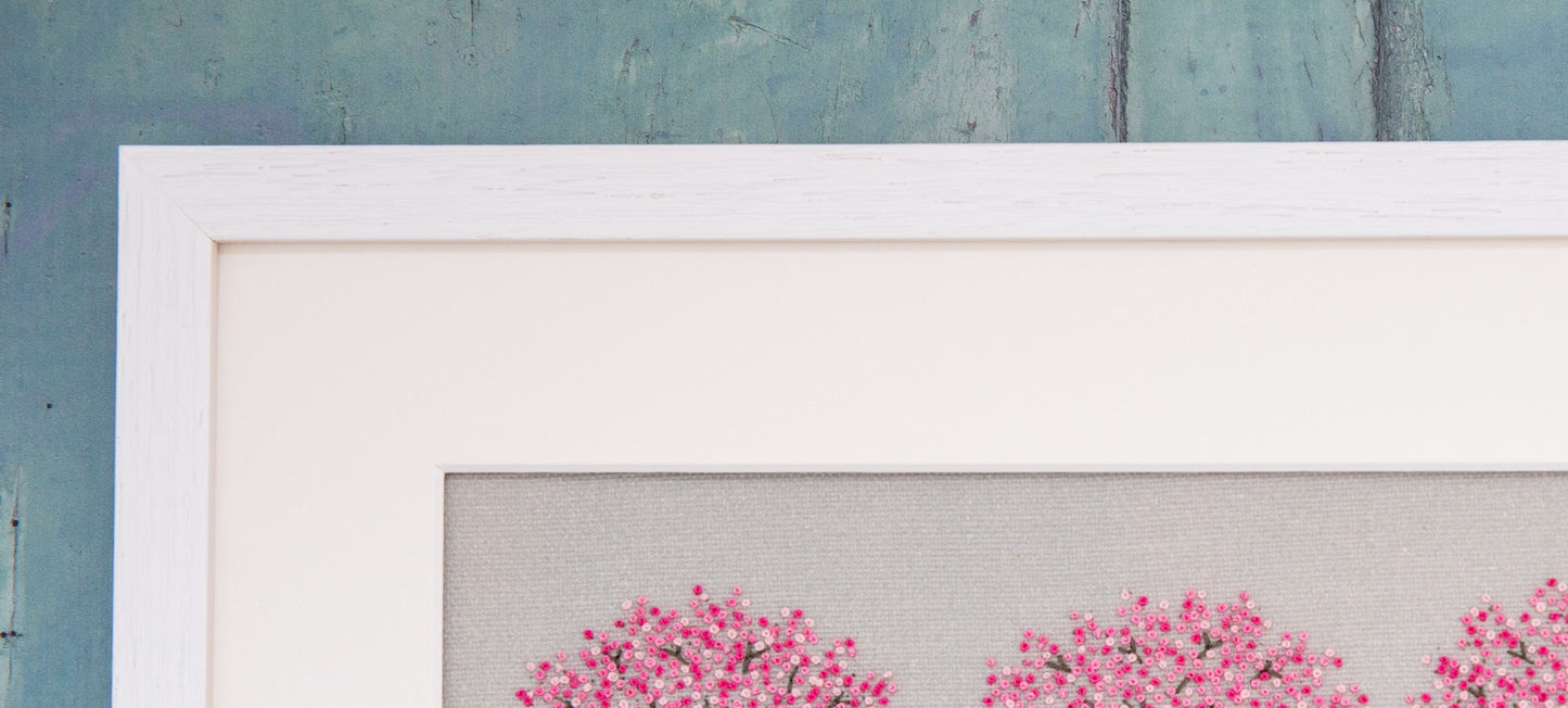 Top left hand corner of a white rectangular frame showing the mount a the top of three hand embroidered cherry blossom trees.