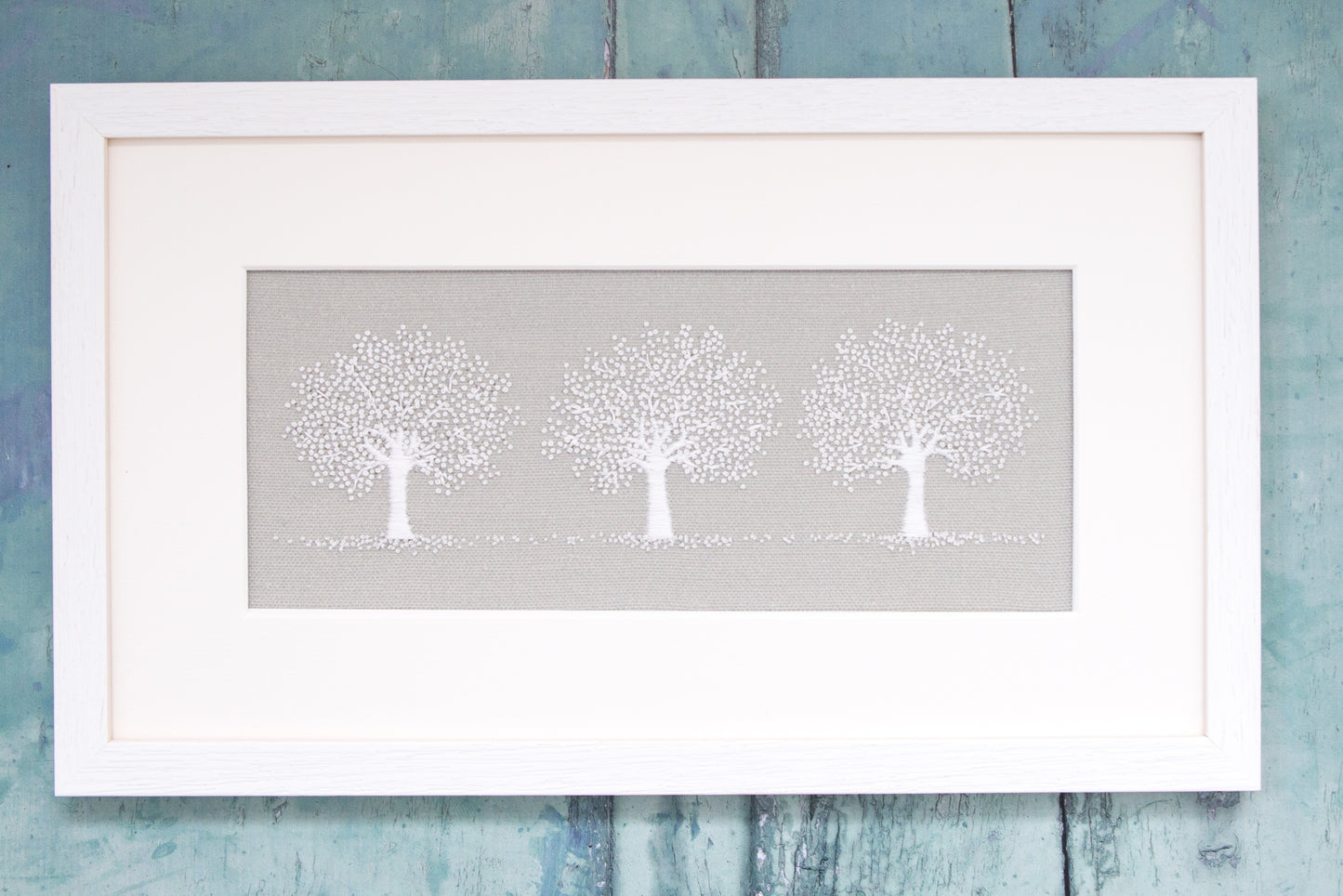 Three white trees sit on a pale grey background in the white framed picture