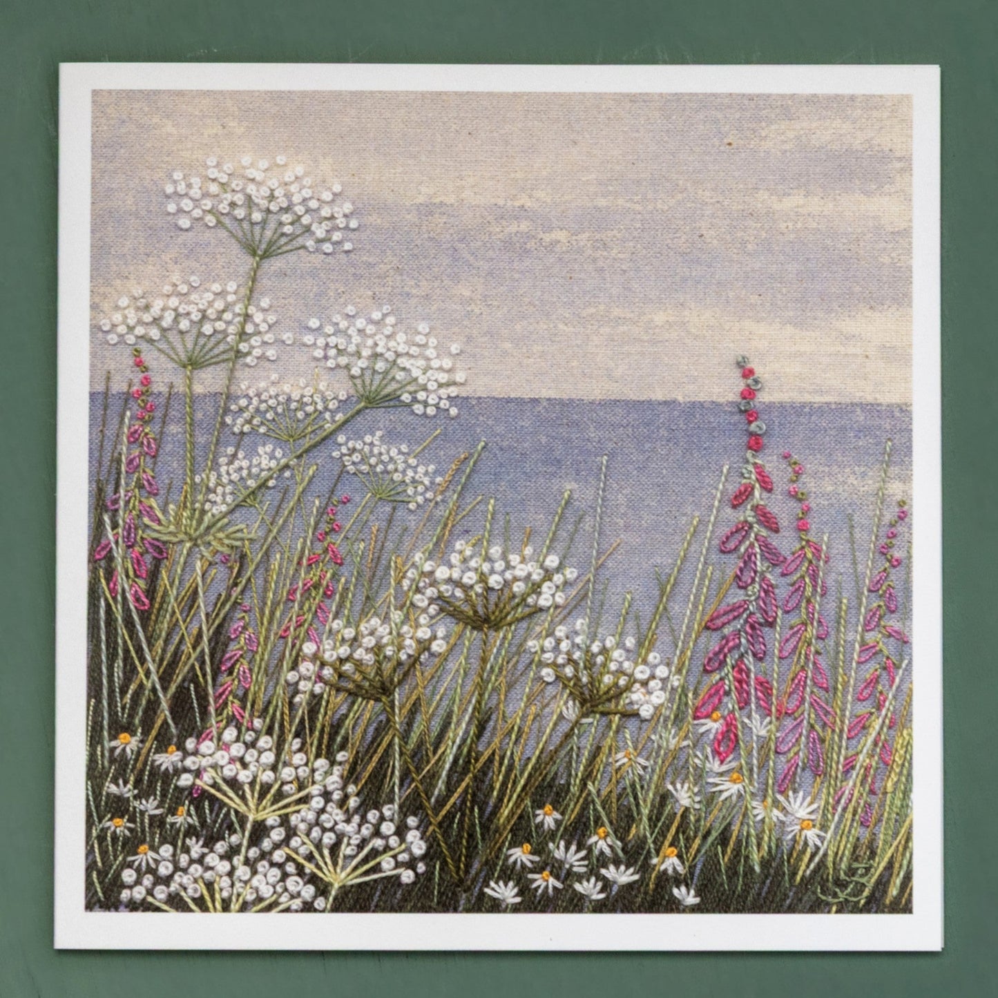 A card of a painted coastal horizon with wild flowers in the foreground.