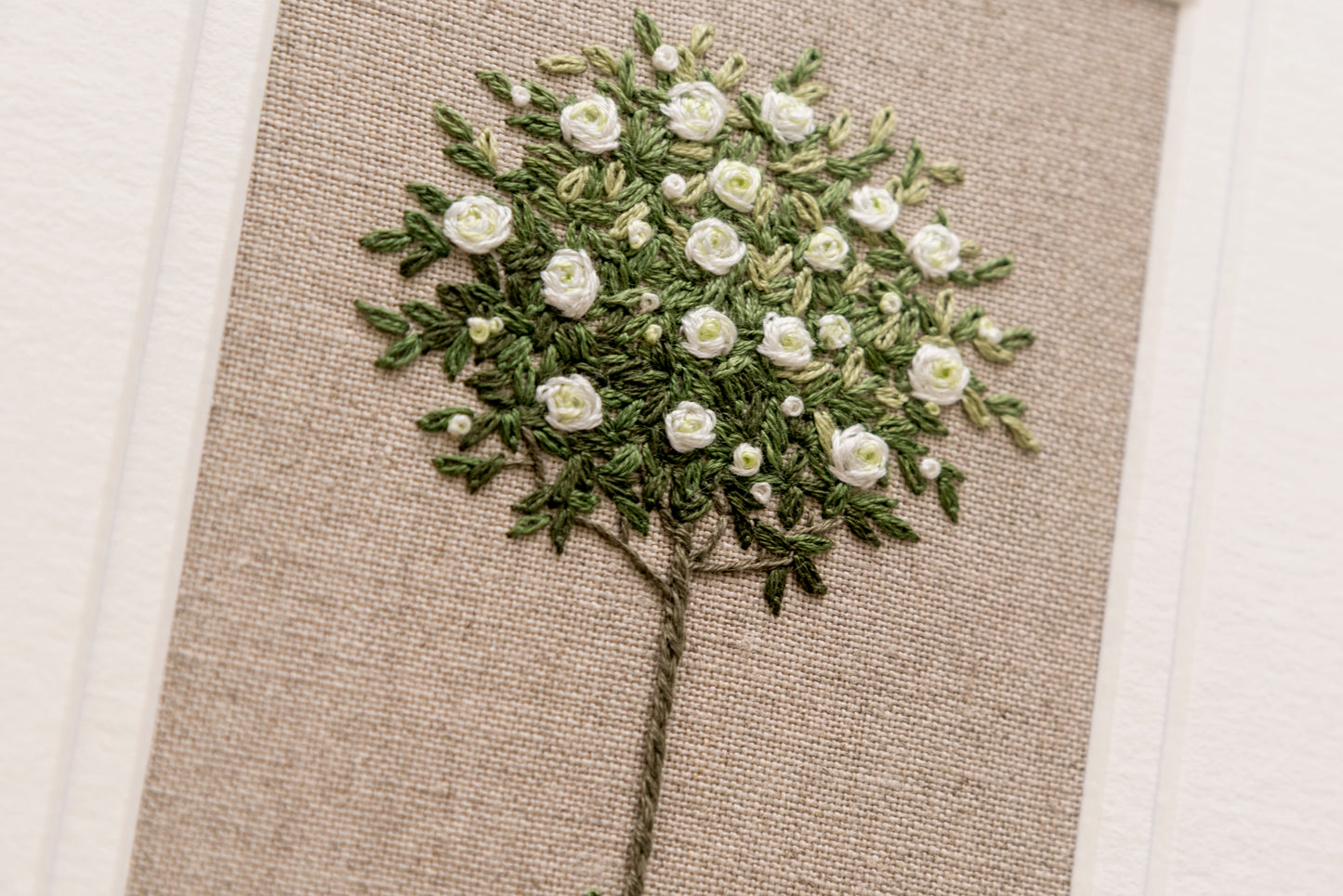 close up of the detail in this hand embroidered white standard rose on beige linen