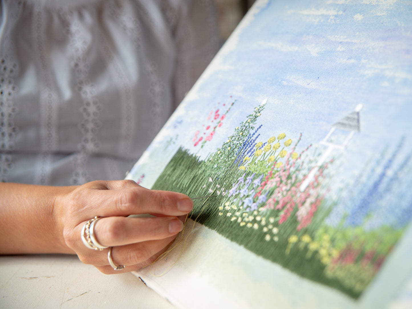 angled close up of Jo's hand embroidering daisies onto the Cottage Garden embroidery artwork.