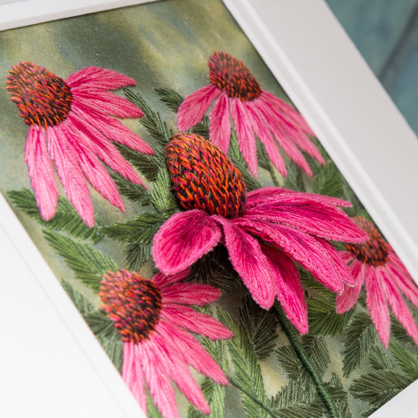 pink echinacea stump work. a large pink 3D cone flower protrudes from the background of other sewn pink cone flowers and their foliage.