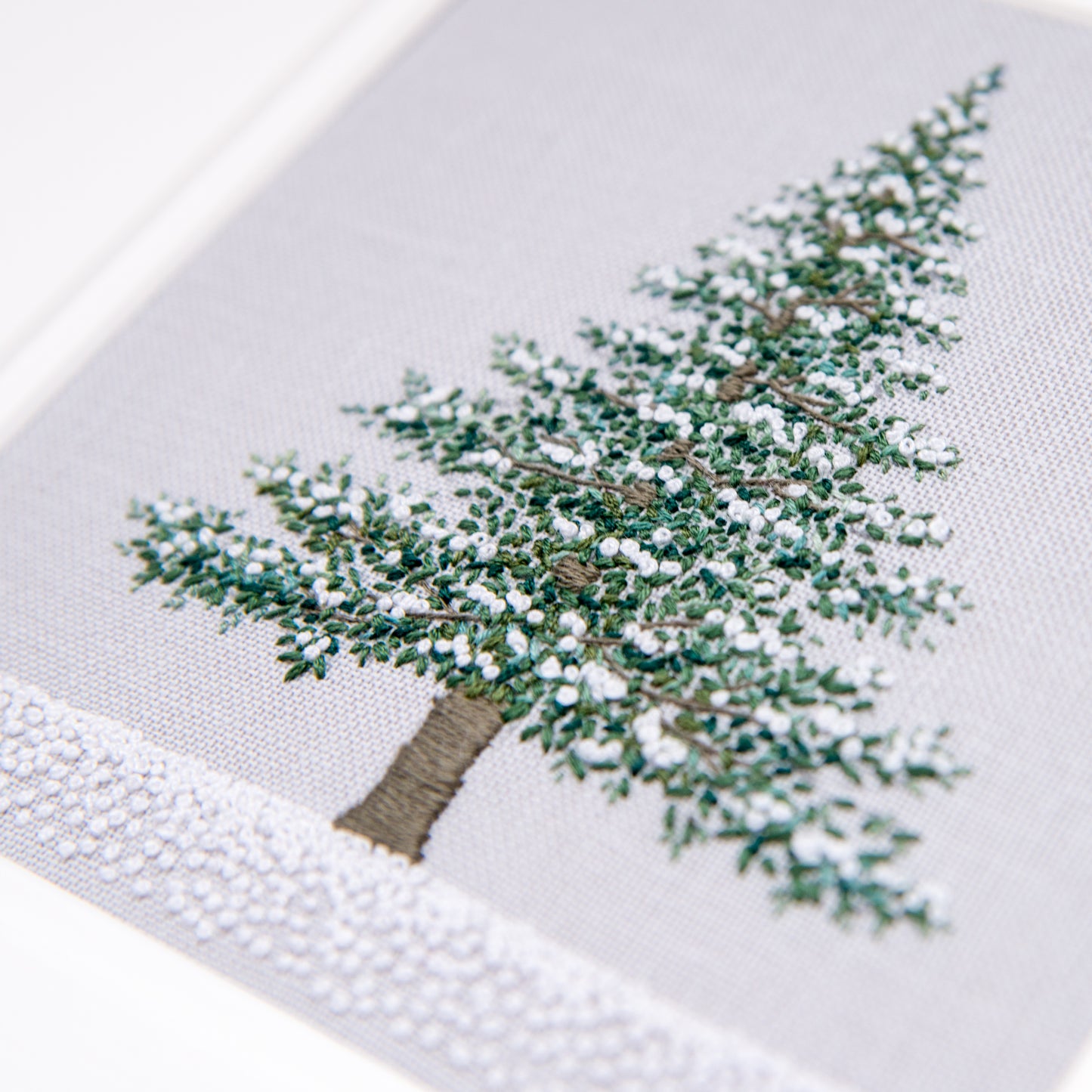 Hand embroidery of a single fir tree with snow on it's branches