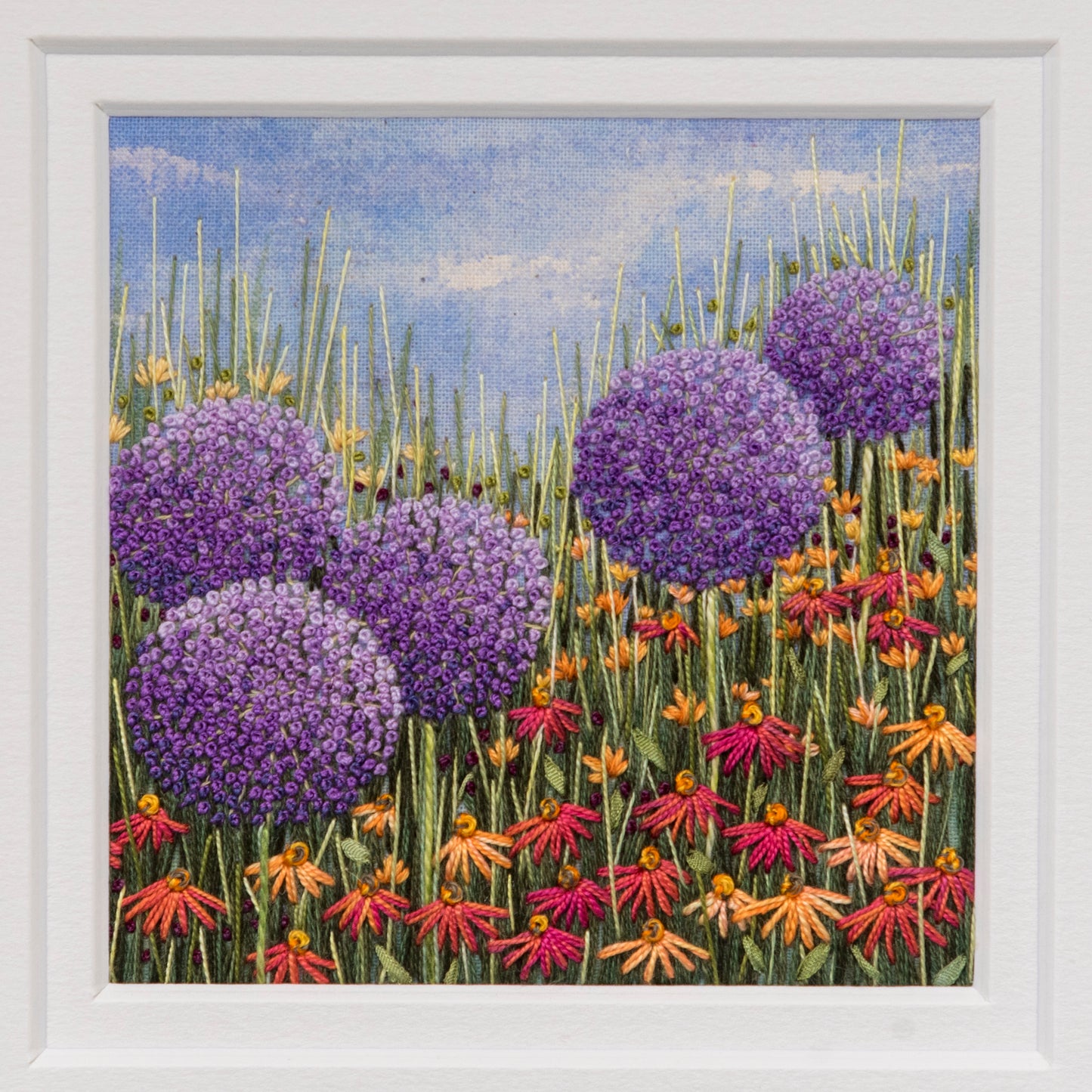 Five large purple allium heads are the main feature of this hand embroiery artwork by Jo Butcher.  
The allium heads are sitting above red/orange daisies, grasses and foliage