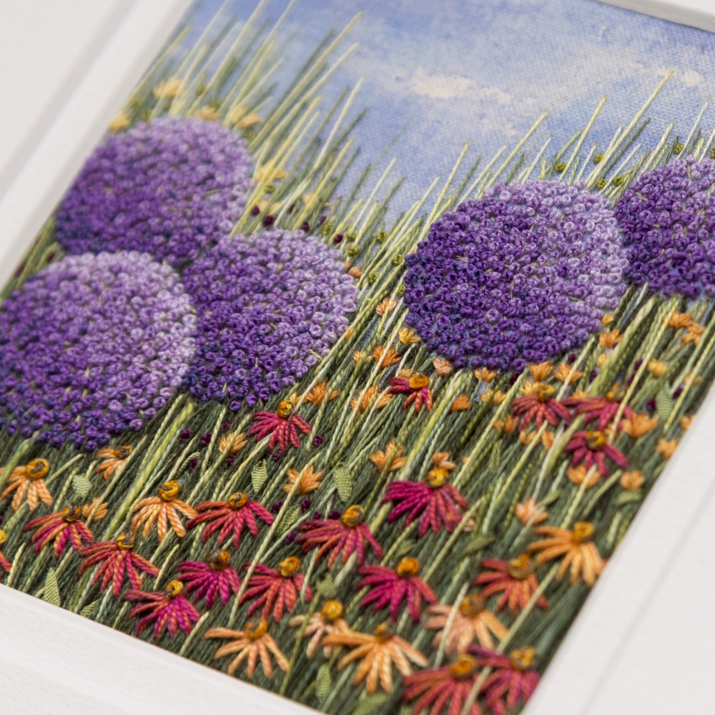 Close up of hand embroidery of alliums with orange and red/orange cone flowers in amongst the foliage