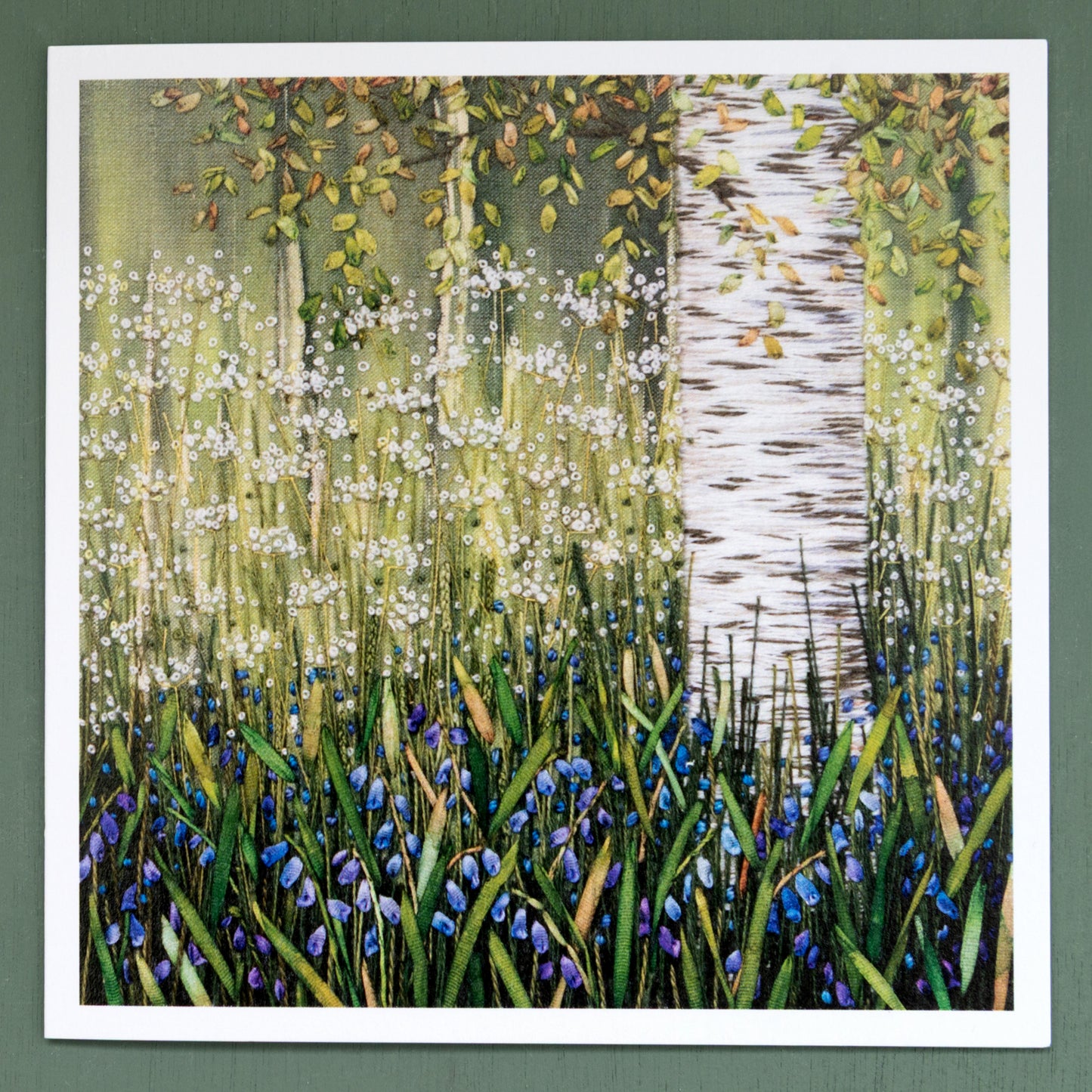 embroidered scene of a birch trunk and lower branches, rising above a carpet of bluebells.
