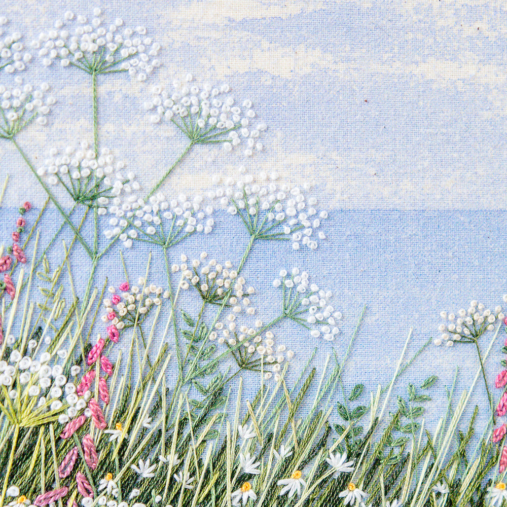 Hand embroidery by Jo Butcher of Cow parsley, daisies and foxgloves in the foreground and the sea and horizon beyond.