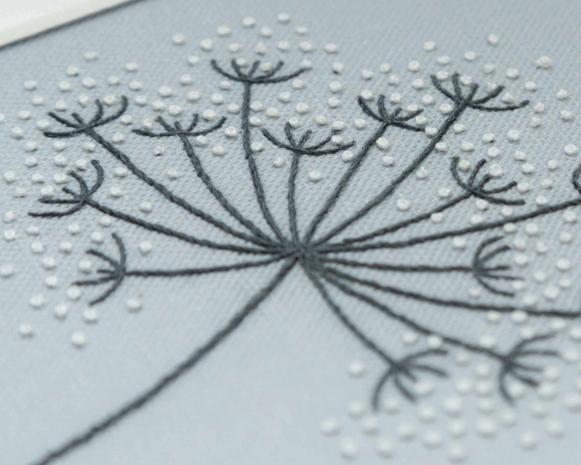 A close up of a cow parsley seedhead hand embroidered by Jo Butcher on a grey linen background