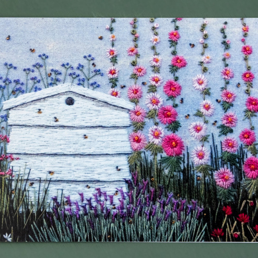 A hand embroidered white bee hive is the main feature if this card.  The bees are flying around the hive and the surrounding flowers.