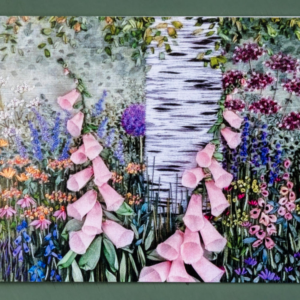 A Card showing the hand embroidered trunk of a silver birch tree. Under the tree is a flower border filled with a range of flowers in full bloom.