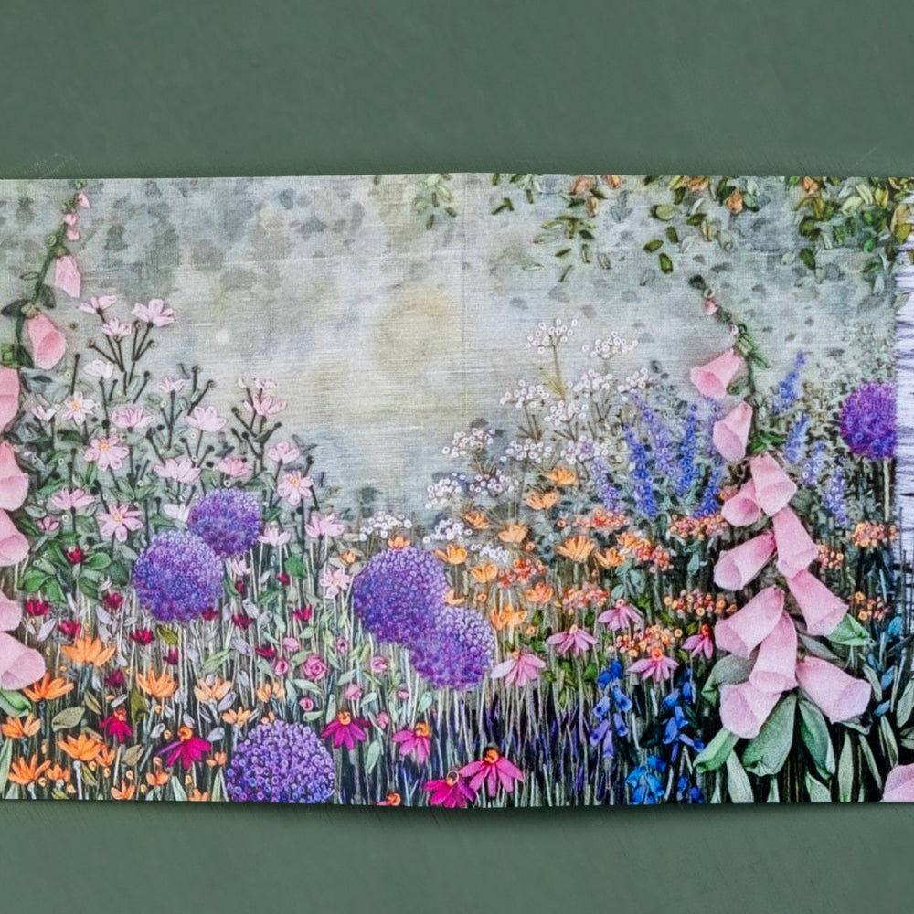 An open card showing the front and back image of a hand embroidered trunk of a silver birch tree. Under the tree is a flower border filled with a range of flowers in full bloom.