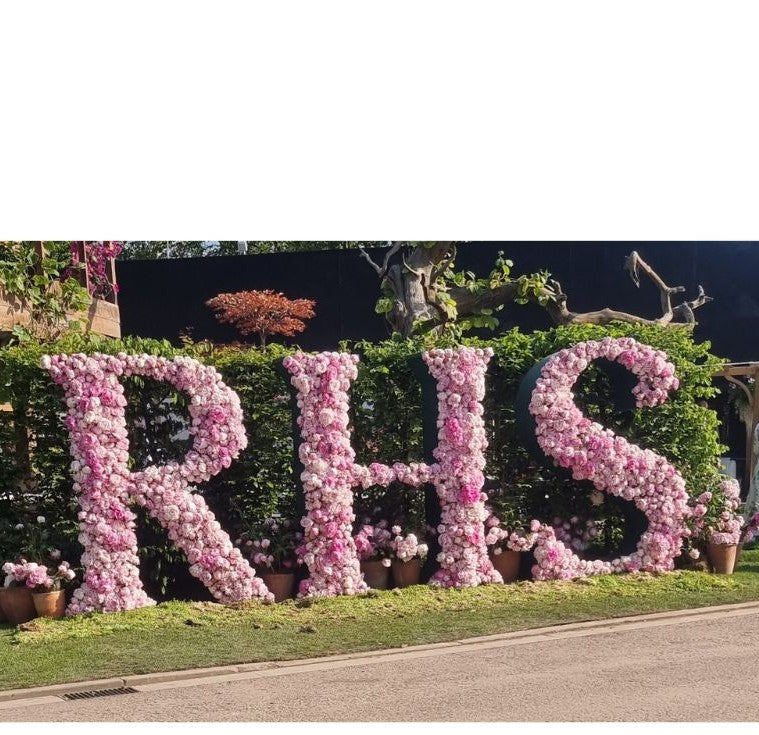 RHS sign made from pink flowers against a green hedge