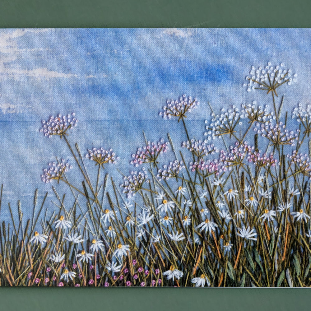 A card of a classic coastal scene. The hand painted  background shows the horizon and the foreground is coastal wild flowers.