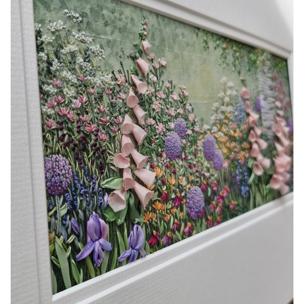view looking across hand embroidery of pale pink foxgloves and other flowers and a silver birch trunk