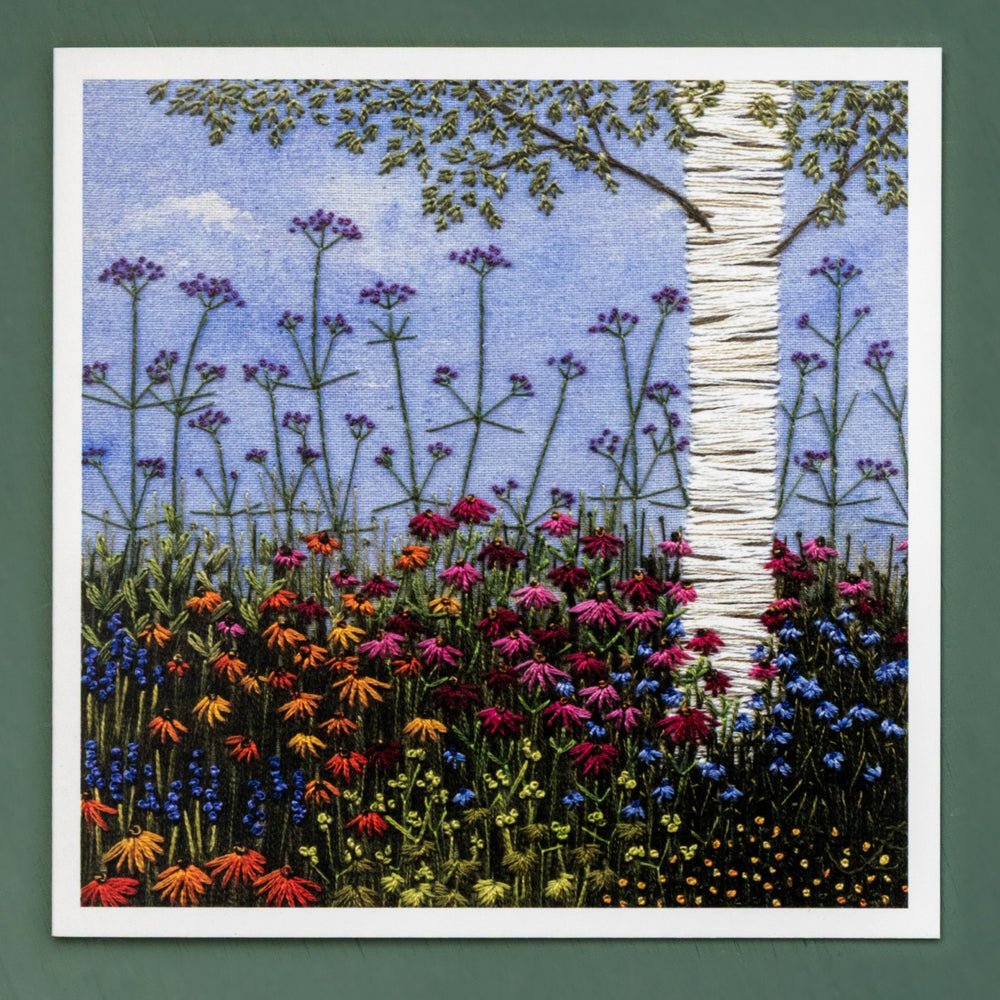 A hand embroidered silver birch tree with lower branches is set in flowering border of deep purple and range echinacea and delicate blue and yellow flowers to contrast.